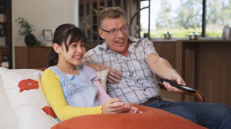 Grandfather and granddaughter together watch interesting entertainment media on TV. Old senior use technology communicate with young generation cross generation gap strengthen family bond. Divergence.