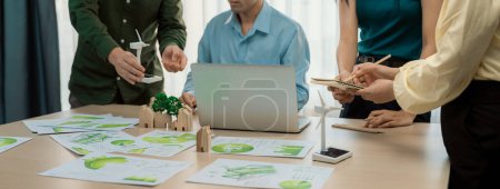 Photo for Cropped image of skilled businessman presented eco-friendly house project to general manager at meeting table with wooden block, windmill model and environmental document scatter around. Delineation. - Royalty Free Image