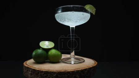 Macrography, a tantalizing margarita is captured in a glass garnished with a vibrant lime slice, all set against a captivating black background. Each close-up shot of cocktail and lime. Comestible.