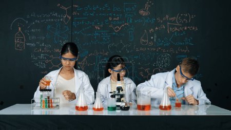 Nettes Mädchen, das unter dem Mikroskop schaut, während Schüler an der Tafel mit Theorie experimentieren. Junge Wissenschaftler inspizieren farbige Lösung am Tisch mit Experimentiergeräten platziert. Erbauung.