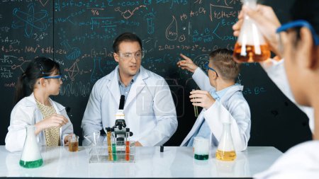 Kluge Lehrer erklären die chemische Theorie, während Schüler farbige Lösungen mischen oder experimentieren. Lehrer, der Chemie unterrichtet, während er im MINT-Unterricht auf die Tafel zeigt. Erbauung.
