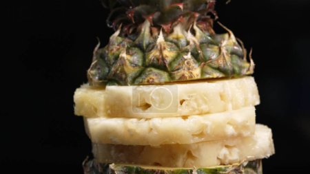 Nahaufnahme Video von frischer Ananas mit Scheibe geschälter Ananas mit separatem schwarzen Hintergrund. Die raue und wachsartige Rinde, mit einer Krone aus stacheligen grünen Blättern, Food-Fotografie. Komestibel.