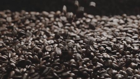 Nahaufnahme fallender Kaffeebohnen mit schwarzem Hintergrund. Zeitlupe. Abstrakte von geröstetem Kaffee fallen zusammen mit einem Haufen Kaffeebohnen, die für die Zubereitung von Kaffeezubereitungsmethode oder Zutaten vorbereitet sind. Komestibel.