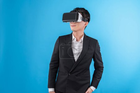 Foto de Un hombre de negocios asiático sonriente que busca una realidad virtual completa conectándose al informe del mundo de los negocios en metáfora futurista, analizando los anuncios de tecnología de innovación en un espacio de copyspace azul aislado de realidad virtual. Aparatos. - Imagen libre de derechos