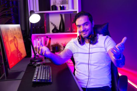 Smart gaming streamer looking at camera with trendy pose, playing battle team shooting gun background at warship on pc screen at side view, using headset at digital neon light studio room. Surmise.