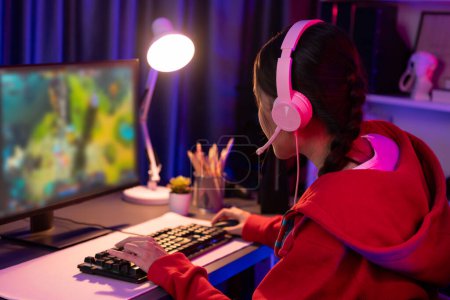 Host-Kanal von jungen schönen asiatischen Gaming-Streamer spielen Kampf Moba in der Schlacht Arena Spiel auf dem PC-Bildschirm mit Multiplay, trägt pastellfarbenen Kopfhörer in Neon-Digitallicht modernen Raum. Stratagem.