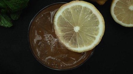 Makro aus einem Tequila Sunrise-Cocktail mit Zitronen- und Minzblättern vor einem dramatischen schwarzen Hintergrund. Nahaufnahme fängt die lebhaften Farben des Cocktails ein. Ansicht von oben. Komestibel.